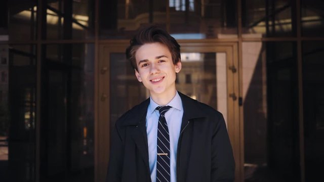Portrait of petty Caucasian boy. wearing classic clothes on background of business center . Gorgeous young man with beautiful smile looking directly at camera. Outdoors.
