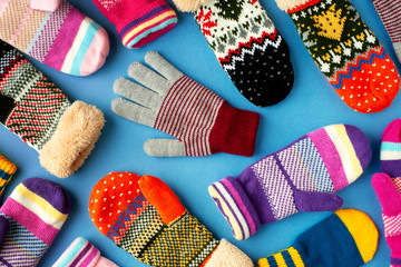 Mittens and gloves are scattered on the table. Multicolored mittens and gloves for autumn and winter. Clothes for the cold seasons on a blue background. View from above. - obrazy, fototapety, plakaty