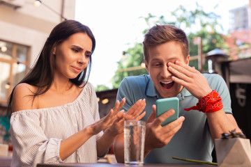 Modern man. Modern man laughing out loud while watching old photos sitting near his stylish beautiful girlfriend
