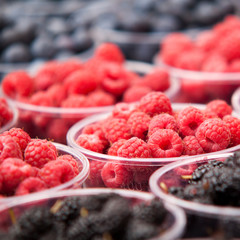 ripe raspberries and blackberries spread out in plastic cups