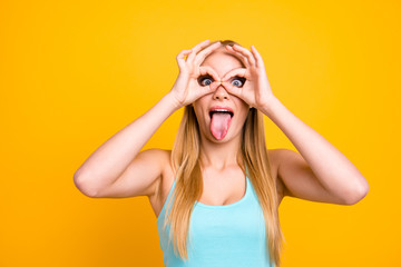 Funny and cheerful girl with long blond straight hair. Female showing gesturing ok sign with her two hands like a glasses and looking at camera, demonstrating tongue out and opened eyes wide © deagreez