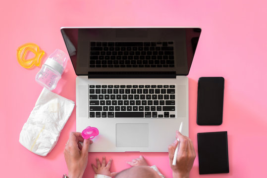 Working mom - young woman holding a baby working at a desk with laptop. flatlay top view
