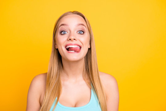 Happy joyful and funky blonde girl showing tongue and make big smile. Attractive young woman is posing on the camera isolated on yellow background
