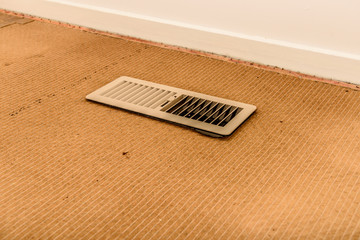 Home cleaning and invisible bacteria concept. Dirty ducted heating system outlet and messy carpet underlay.