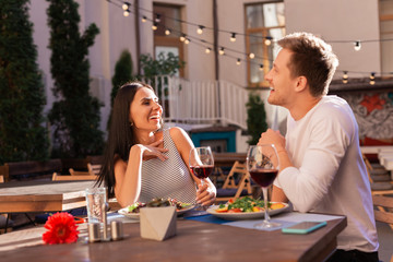 Fancy terrace. Dark-haired appealing woman laughing out loud with her handsome man while sitting on fancy summer terrace