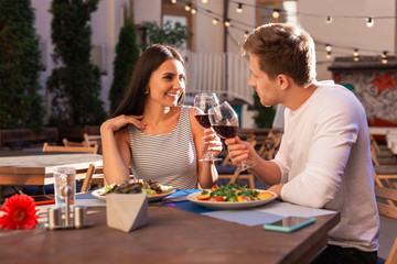 Clanging glasses. Elegant young woman wearing fashionable tight dress clanging glasses with her caring man
