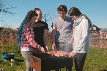 Group of young people friends Barbecue shashlik meat on top of charcoal grill on backyard. Talking and smiling together.