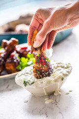 Roasted chicken legs in woman hand and tzatziki dressing.