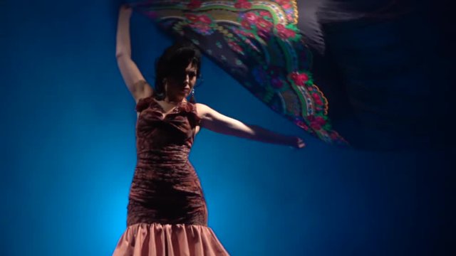 Flamenco. Girl is dancing with a manton in her hands . Light from behind. Smoke blue background. Slow motion