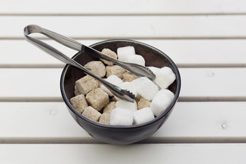 Brown and white sugar cubes in a bowl on a wooden table at cafe