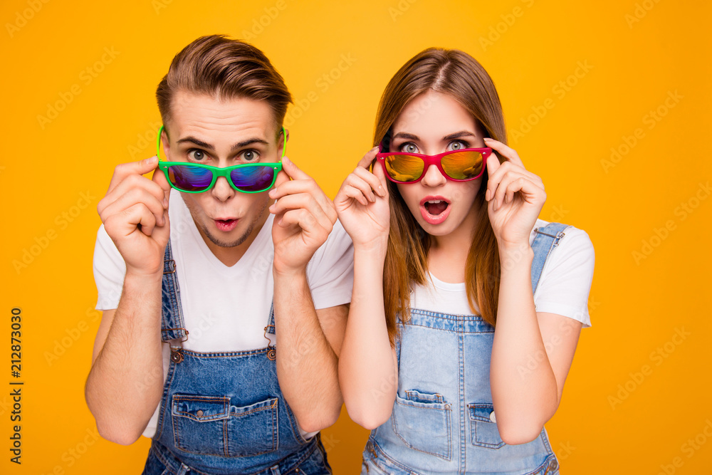 Wall mural Beautiful cute adorable surprised couple putting colorful 3d spectacles down showing wow emotion over yellow background, isolated