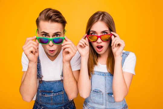 Beautiful cute adorable surprised couple putting colorful 3d spectacles down showing wow emotion over yellow background, isolated
