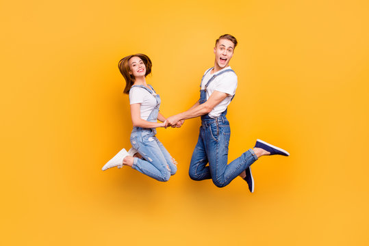 Full length portrait of beautiful attractive playful cheerful, comic couple in casual outfit, jeans, shirts jumping in the air on yellow background, isolated