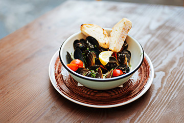 Wooden table. Nice fancy seafood dish with mussels and some bread in creamy sauce standing on the wooden table