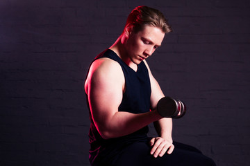Fototapeta na wymiar young handsome man engaged with a dumbbell in the gym on a black brick background