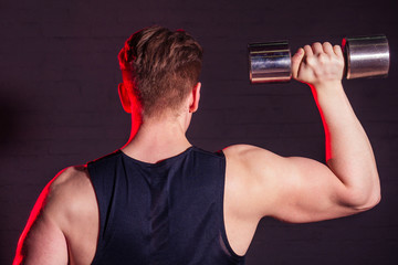 Fototapeta na wymiar young handsome white man in black T-shirt is engaged and posing with dumbbells on a black brick background. The idea of cardio training