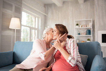 Anticipating daughter. Caring loving mother feeling warm and protected while kissing her anticipating daughter