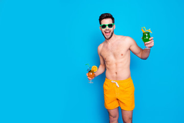 Beach style! Attractive and cheerful man in yellow shorts and eyeglasses, holds cocktails with...