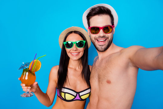 Self portrait of couple with coctail on beach vacation in modern eyeglasses headwear shooting selfie on front camera having beaming smiles isolated on blue background.