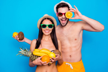 Handsome couple in in a good mood and colourful eyewear holding a lot of fruit. Funky young woman...