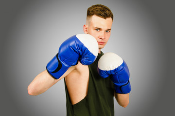 Young guy boxer in blue boxing gloves isolated on a gray background.