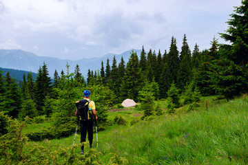 Fototapeta na wymiar Adventurer with backpack walks along green mountain meadow