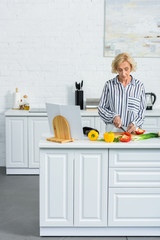 attractive grey hair woman cooking in kitchen and cutting vegetables