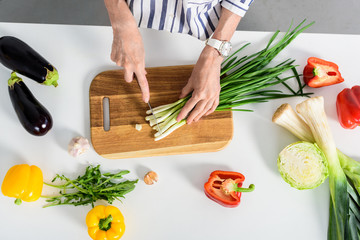 cropped image of senior woman cutting green onion in kitchen