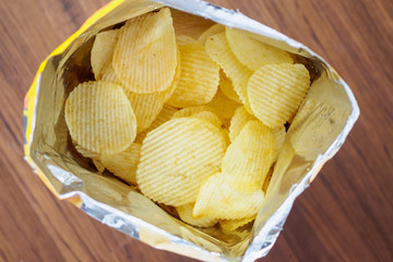 Potato chips in open snack bag close up on table floor