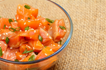 Hawaiian salmon poke with green onions and sesame seeds in glass bowl