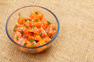Hawaiian salmon poke with green onions and sesame seeds in glass bowl