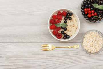 Oatmeal porridge in porcelain bowl with currant berries and raspberries, decorated with mint leaves