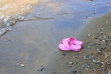 Fototapeta na wymiar children's pink rubber slippers left on the seashore