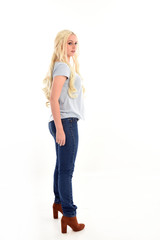 full length portrait of blonde girl wearing simple blue shirt and jeans, standing pose. isolated on white background.