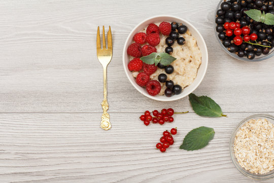Oatmeal porridge in porcelain bowl with currant berries and raspberries, decorated with mint leaves