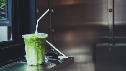 Green tea matcha atte in plastic cup with glasses by the windiw in cafe.
