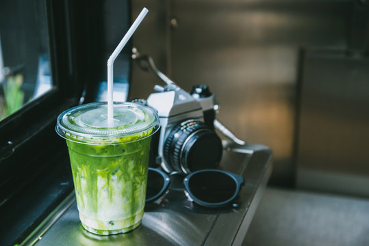 Green tea matcha atte in plastic cup with camera and glasses by the windiw in cafe.
