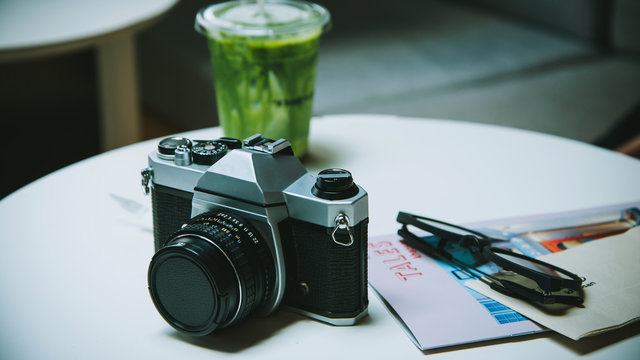 Camera wirh Green tea matcha atte in plastic cup and glasses and travel book on the table in cafe.