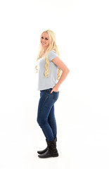 full length portrait of blonde girl wearing simple blue shirt and jeans, standing pose. isolated on white background.