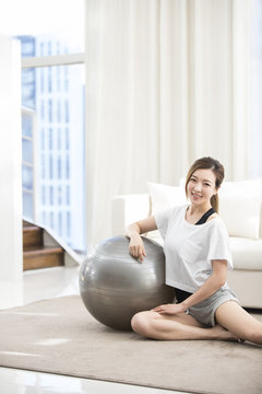 Cheerful young Chinese woman leaning on fitness ball