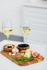 close-up view of glasses of wine and delicious snacks on wooden board on table