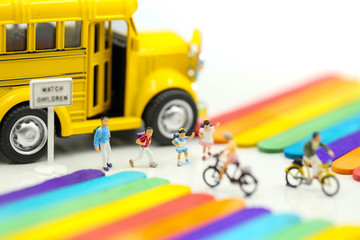 Miniature people : cycling of school bus  with Colorful ice cream sticks background.