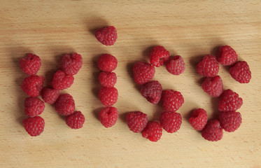 Word kiss laid out of ripe raspberries on a wooden board