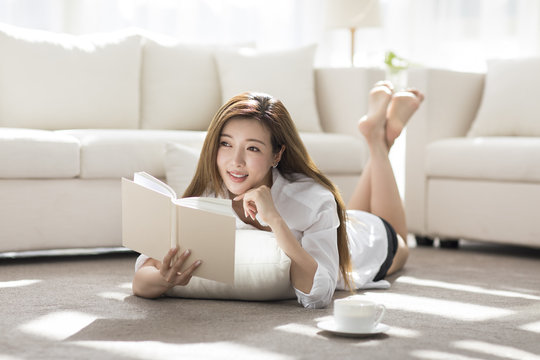 Cheerful young Chinese woman reading a book at home