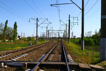 Rail road on country side in summer with a lot of electric poles on it sides on blue sky background