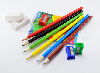 Fototapeta premium Colorful pencils with erasers, sharpener and note pad on white background.