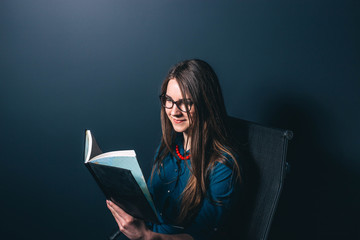 intelligent young woman reading a book on a dark background.