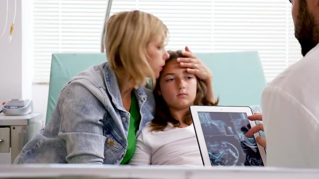 Mother of patient girl talking with doctor while he is looking at MRI results on tablet PC screen