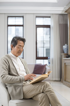 Senior Chinese man reading a book at home