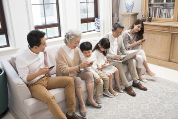 Happy Chinese family using digital devices on sofa